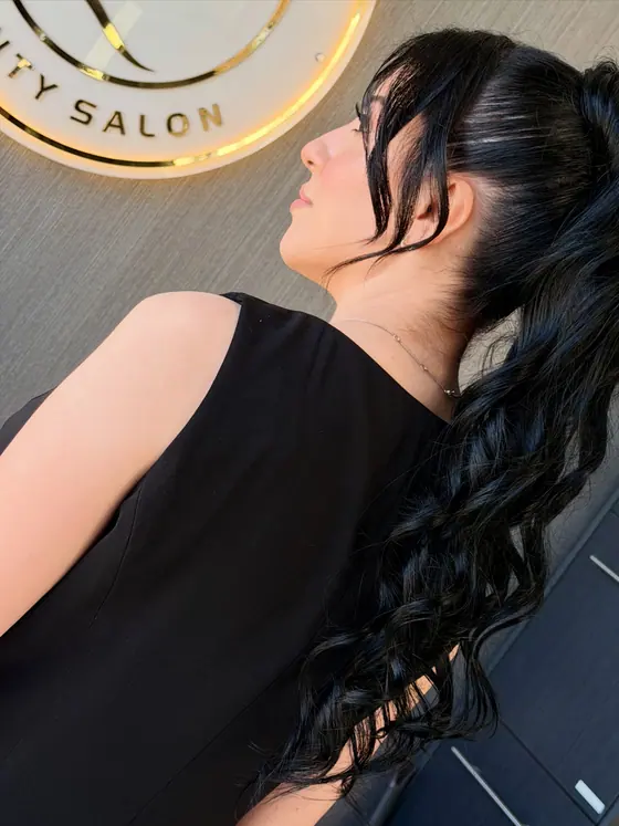 Long dark ponytail with loose curls and face-framing strands